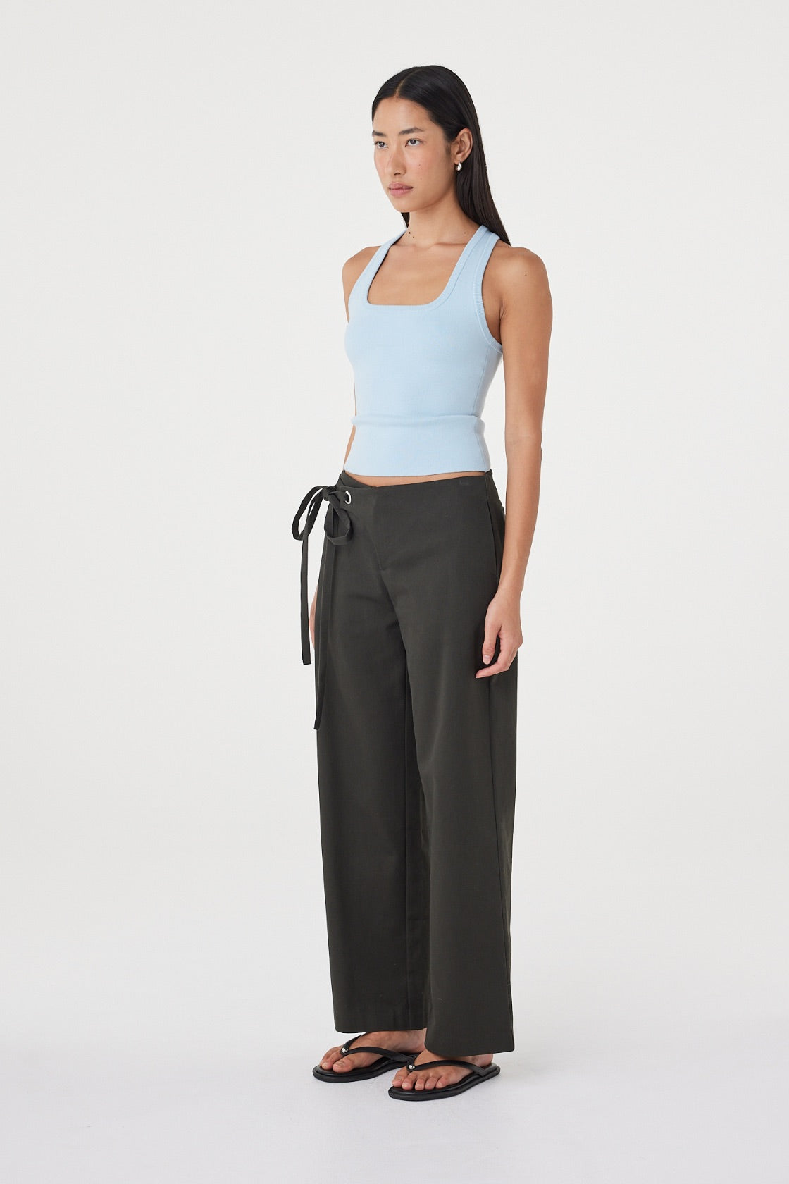 Side view of the Sable Top in Pale Blue showing the streamlined silhouette and fitted shape, styled with charcoal wrap-detail trousers.