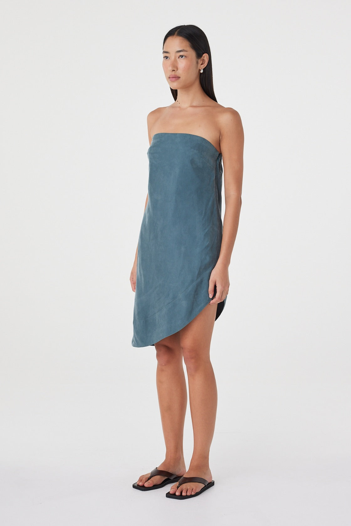 Angled front view of the Rhea Dress in Teal worn on its own, showcasing the strapless shape and asymmetric midi hem.