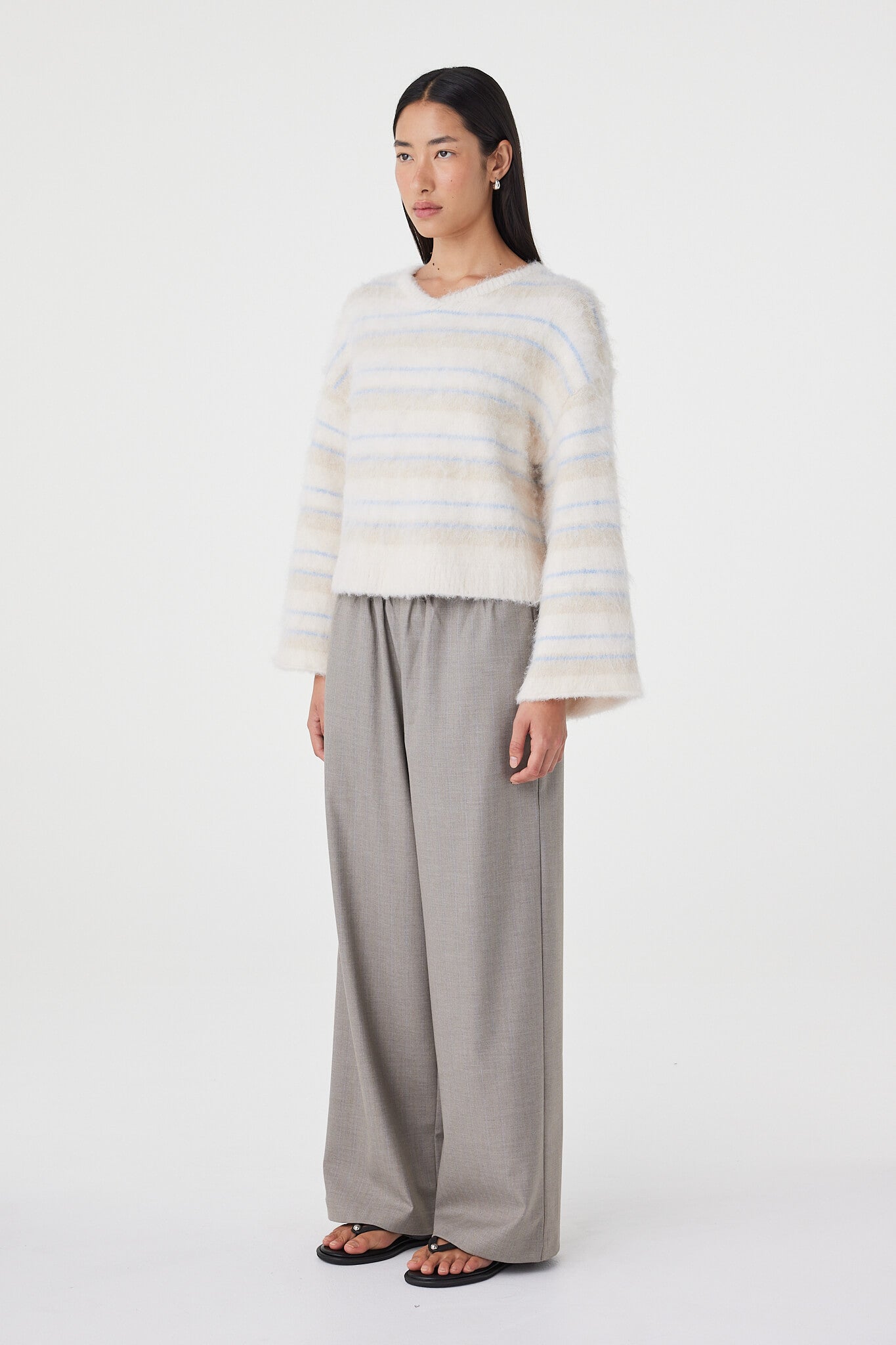 Side profile view of the Lucca Sweater in taupe and blue stripe highlighting the dropped shoulder shape, wide sleeves and soft drape through the body paired with taupe relaxed pants