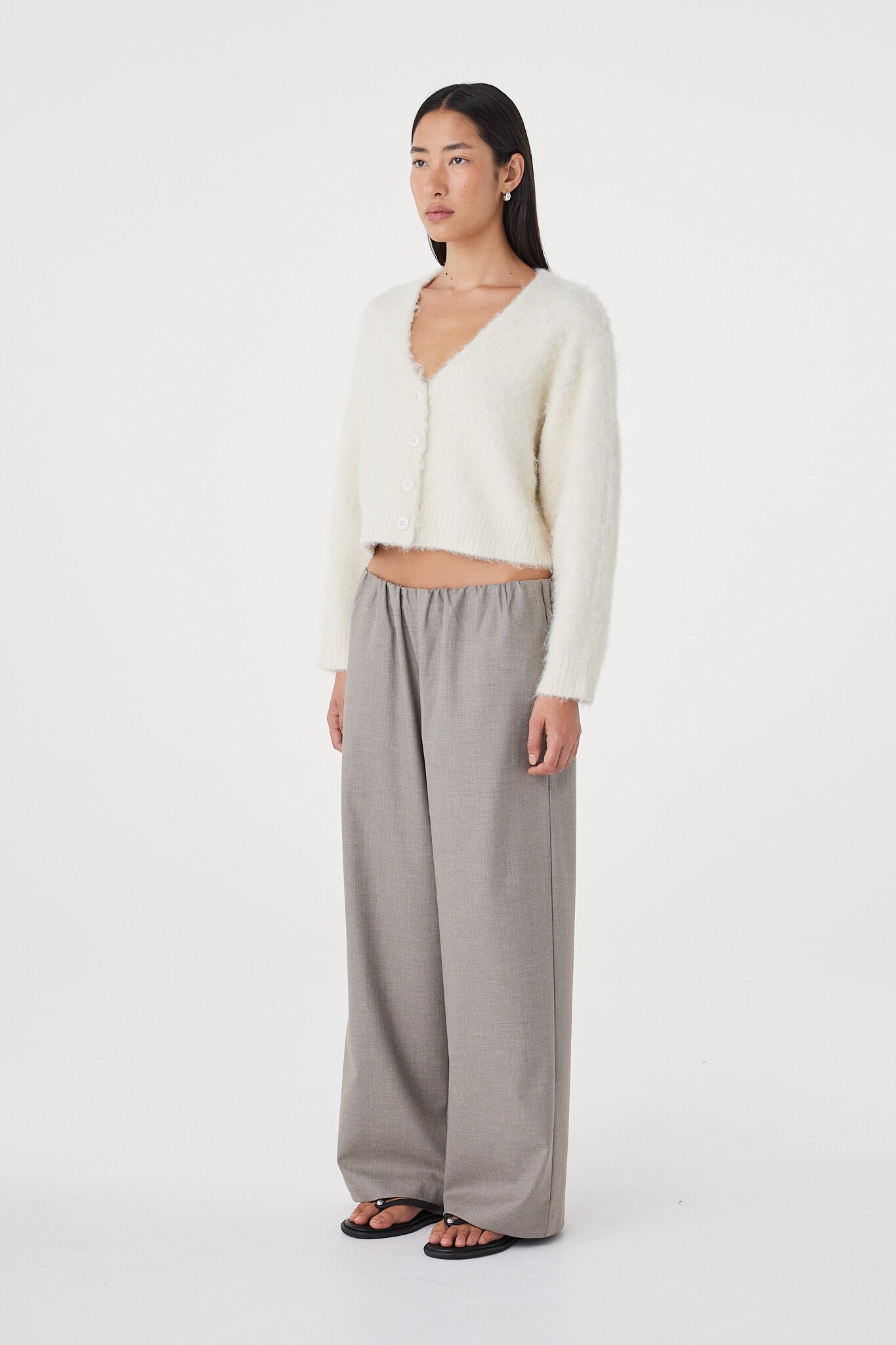 Side profile view of the Liora Fluffy Cardigan in cream paired with taupe wide-leg pants and black sandals, highlighting the dropped shoulder shape and soft fluffy texture