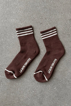 Pair of brown socks with white stripes and text on a gray surface
