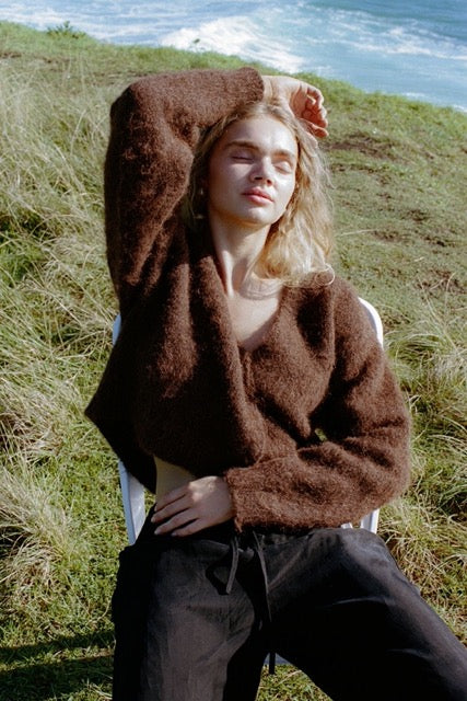 Lifestyle image of brown cardigan worn outdoors sitting on a chair in the grass