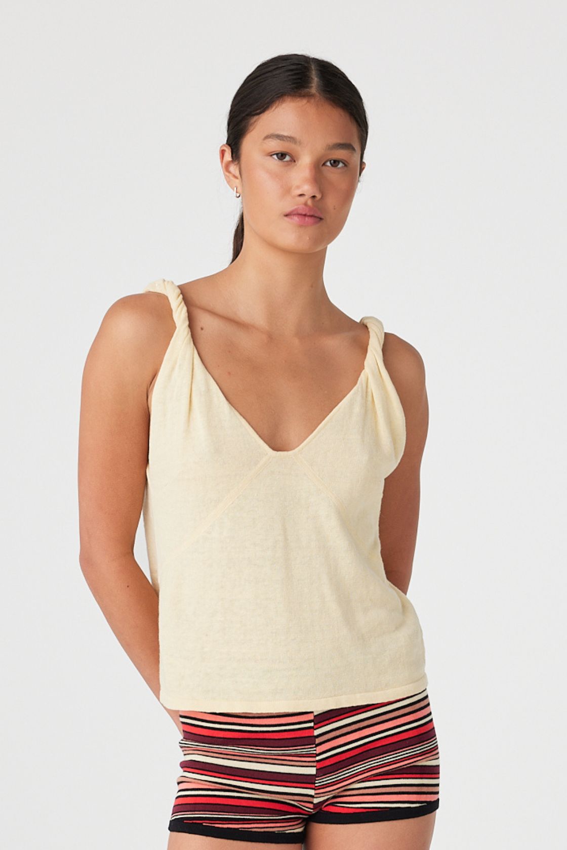 Model in butter yellow linen tank with V-neckline and twist strap detail, styled with striped shorts