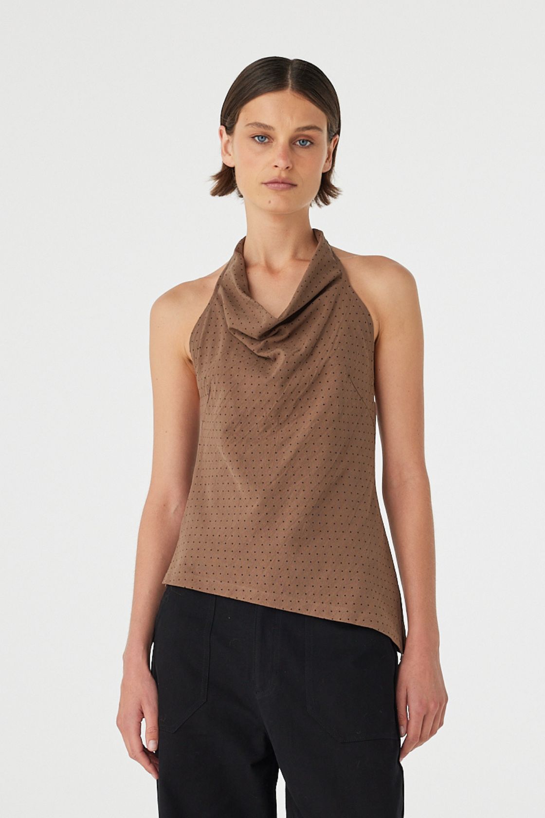 Model wearing Alessia Top in choc polka dot, cotton halter cowl neck top with low back and asym hem, close front view.