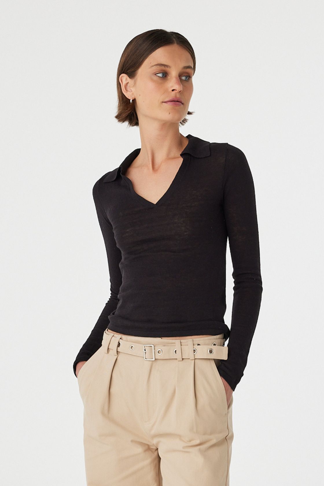 Mae long sleeve top in black worn at an angle with hands in pockets, showcasing the fitted silhouette, collar neckline and soft knit texture, styled with beige pants and sandals