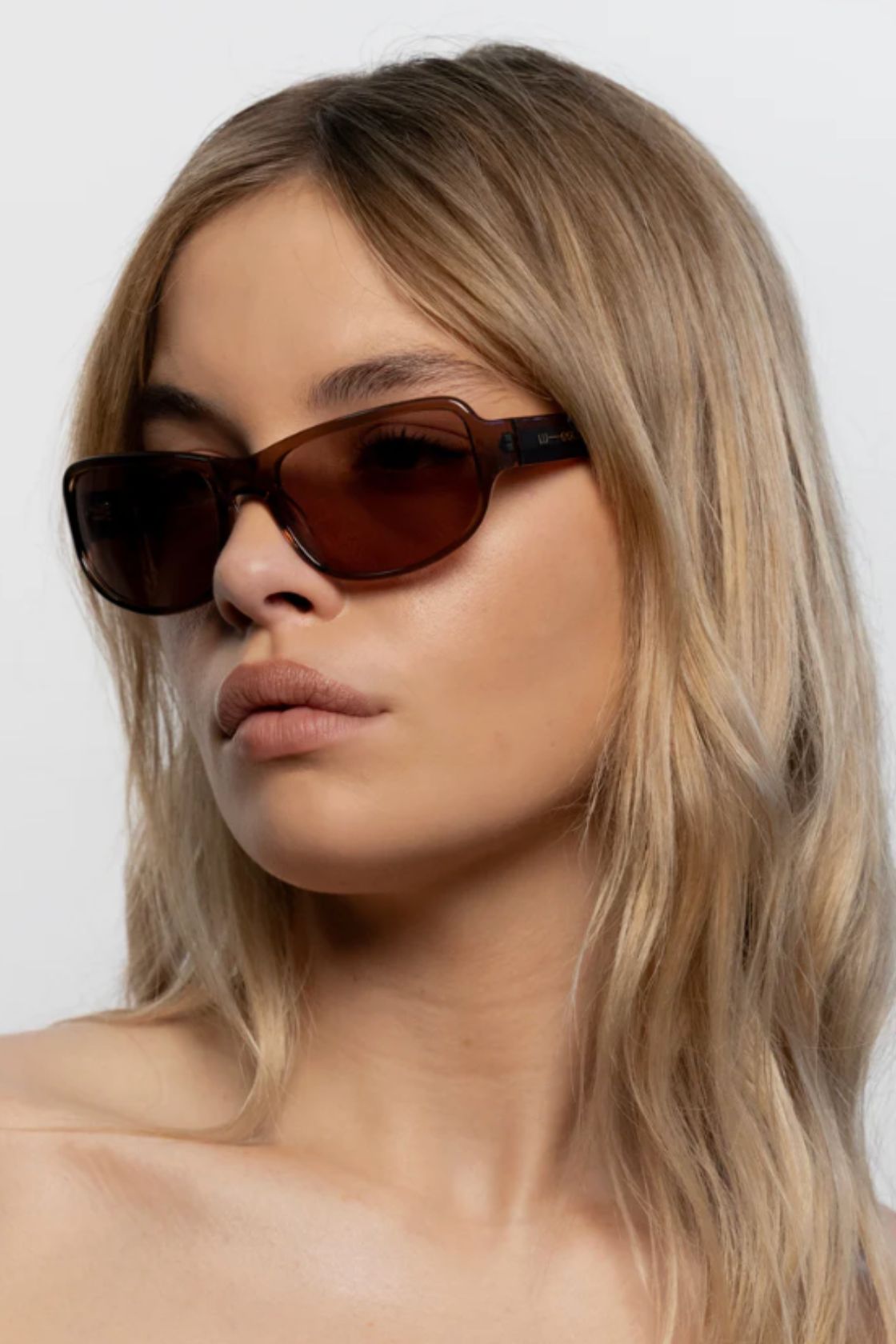 Close up of model wearing coffee tinted rectangular sunglasses with slim acetate frame and neutral makeup look