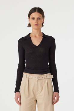 Close up of Mae longsleeve top in black worn front on, showcasing the slim fit silhouette, semi sheer knit texture and V neckline with polo collar, styled with beige wide-leg pants 