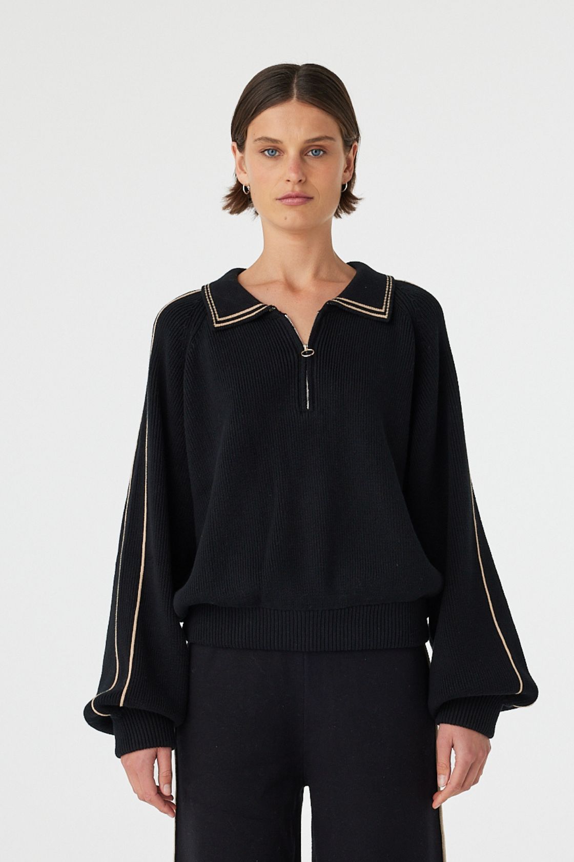 Nella zip sweater in black and taupe worn front on, showcasing the relaxed fit, contrast piping along the collar and sleeves and 1/4 zip detail, styled with matching black wide-leg pants 