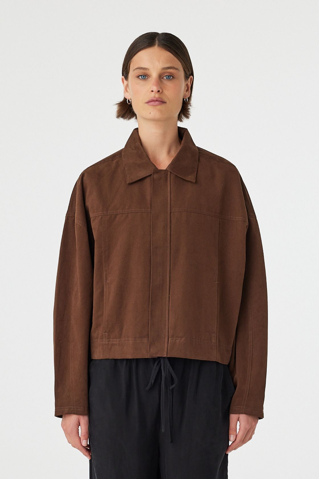 Eames jacket in espresso worn front on, showcasing the cropped boxy fit, clean front panel and concealed zipper, styled with black wide-leg pants