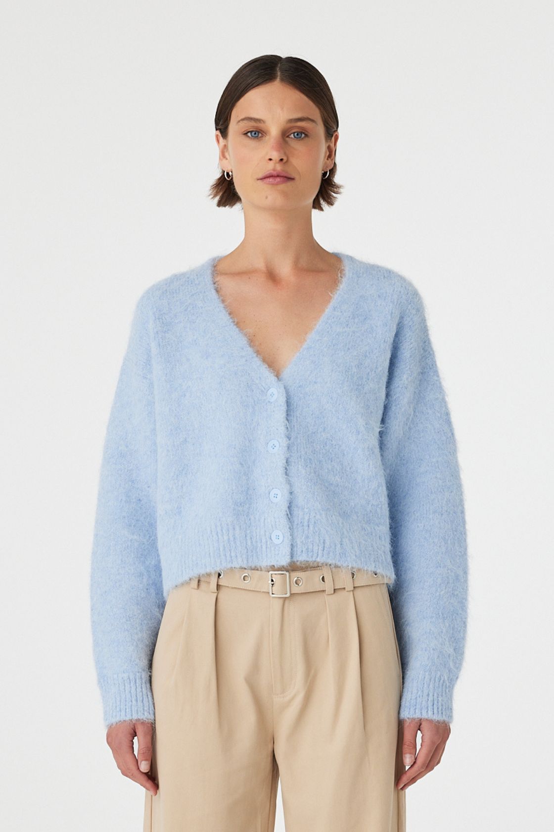 Liora fluffy cardigan in sky worn front on, featuring a button-up front, cropped length and relaxed silhouette, styled with beige trousers 