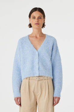 Liora fluffy cardigan in sky worn front on, featuring a button-up front, cropped length and relaxed silhouette, styled with beige trousers 