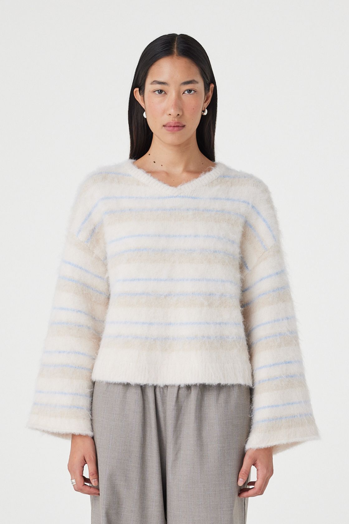 Front view of the Lucca Sweater in taupe and blue stripe featuring a soft fluffy knit texture, relaxed cropped silhouette and deep V-neckline styled with relaxed taupe pants