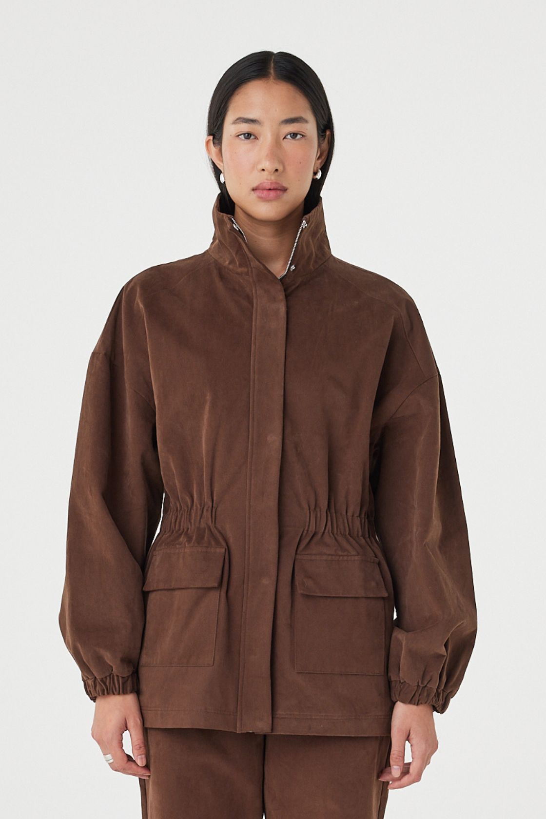 Amari Jacket in espresso with a soft velvet finish, styled with matching straight-leg pants, featuring oversized flap pockets and a high funnel neckline