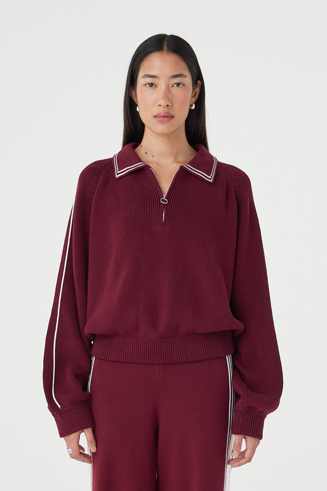 Front close-up view of the Nella Zip in merlot and cream featuring contrast piping along the collar and sleeves, a silver 1/4 zip closure and ribbed waistband detail styled with matching knit pants
