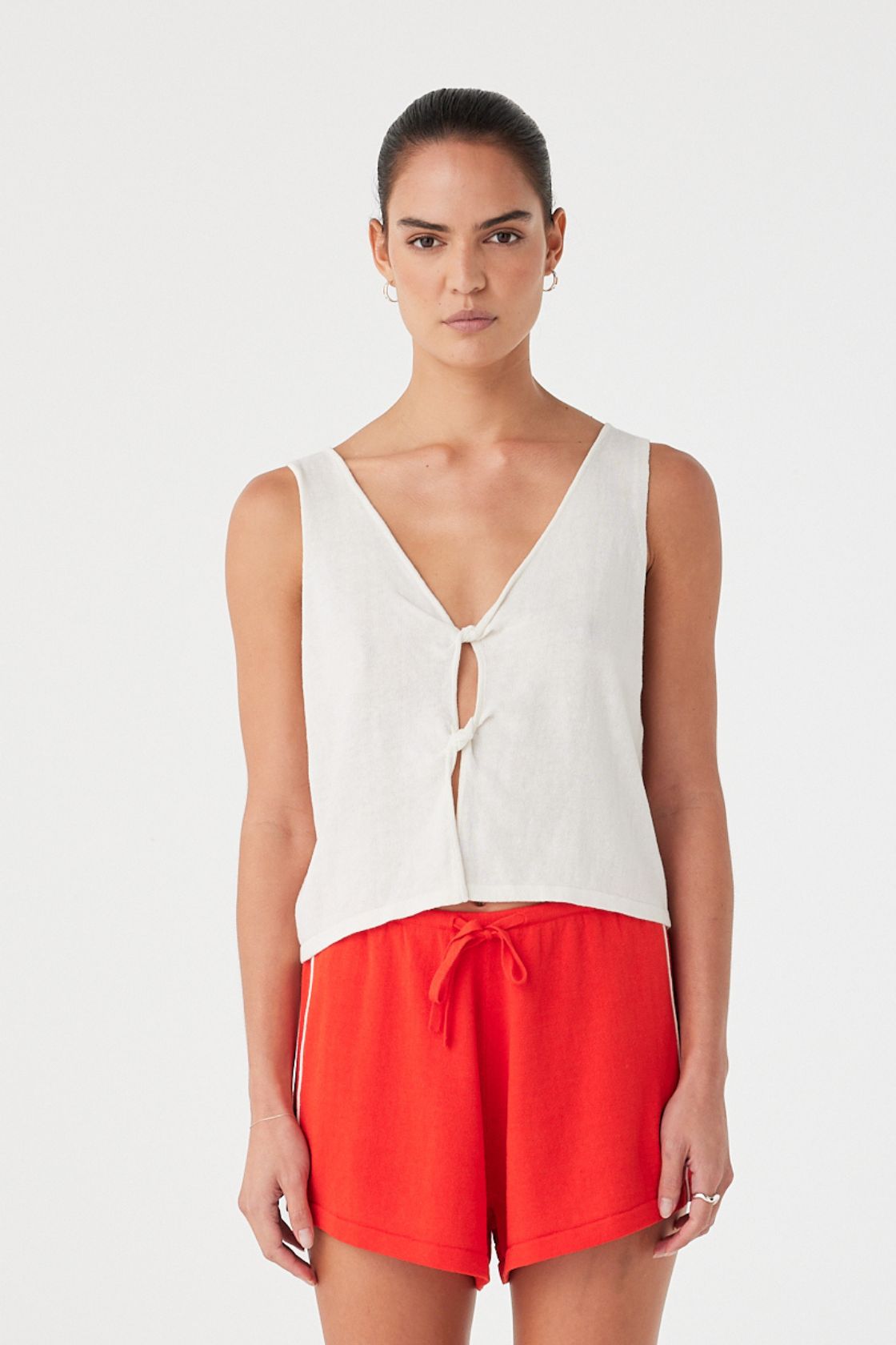 Model wearing cream tank with a relaxed boxy fit and twist-front cutout, in linen–cotton knit for warm weather use.