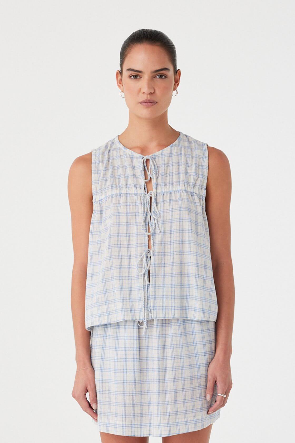 Model wears powder blue check blouse with front tie closures and ruched yoke. Relaxed cotton fit with airy texture.