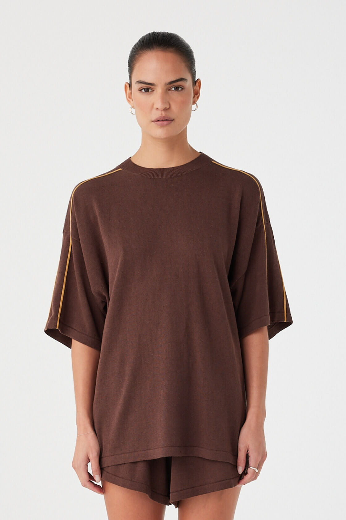 Model wearing oversized espresso linen–cotton tee with drop shoulders and contrast stripe detail.