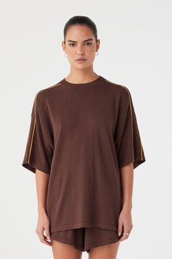 Model wearing oversized espresso linen–cotton tee with drop shoulders and contrast stripe detail.