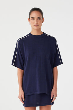 Model wearing navy oversized tee in linen–cotton blend with white contrast stripe along shoulders. Relaxed fit with dropped sleeves.