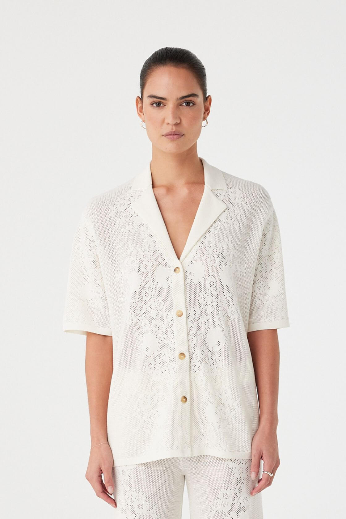Woman wearing a white lace blouse with gold buttons on a white background