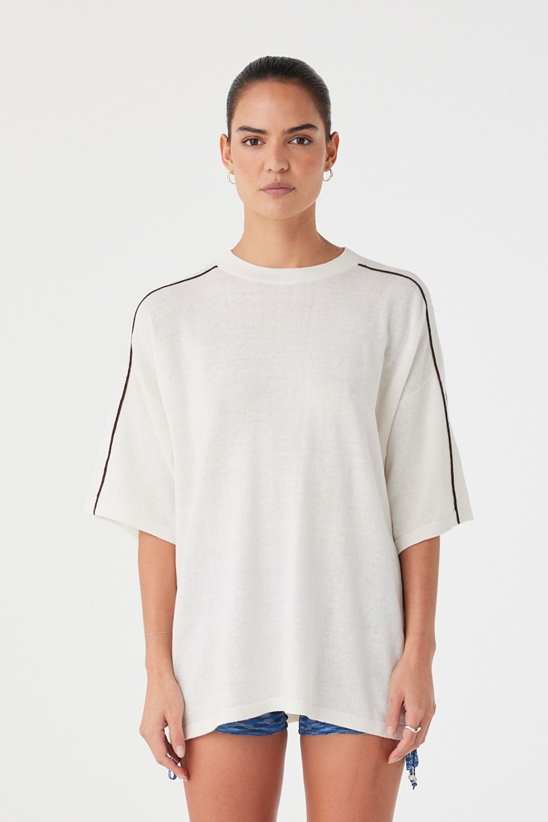 Model wearing cream oversized knit tee with black contrast stripe on sleeves. Linen–cotton blend with soft drape and dropped shoulders.