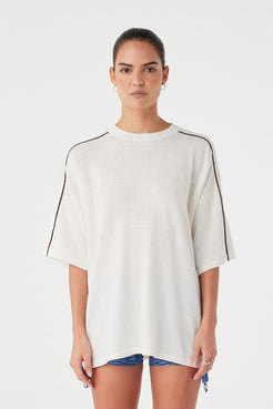 Model wearing cream oversized knit tee with black contrast stripe on sleeves. Linen–cotton blend with soft drape and dropped shoulders.