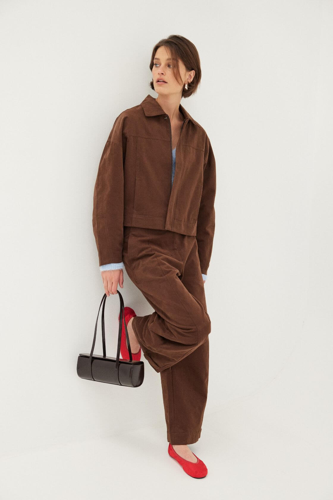 Structured brown two piece set with cropped jacket and relaxed trousers, styled with red flats and black handbag
