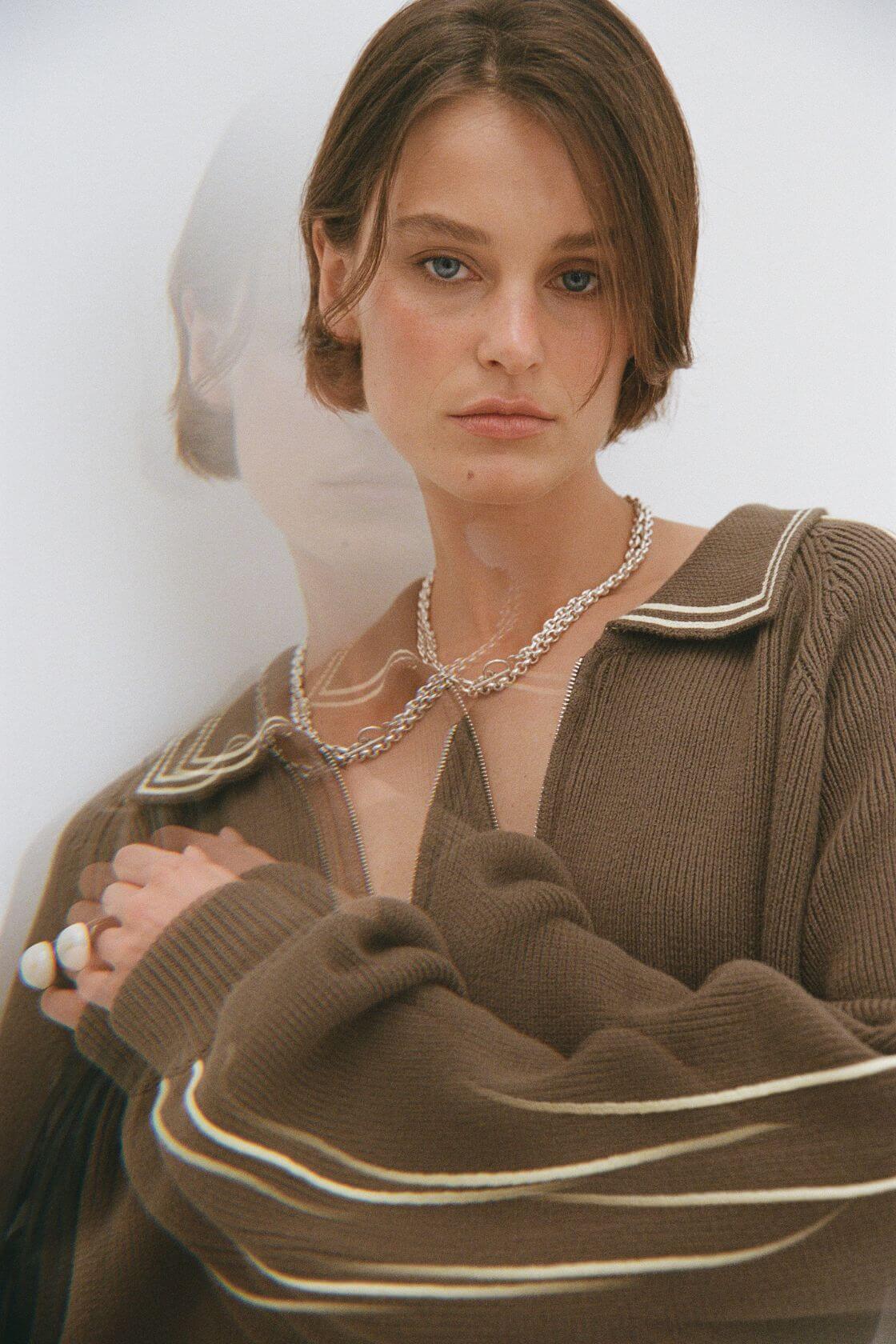Close up of brown zip knit with contrast trim and silver chain jewellery, ribbed texture detail