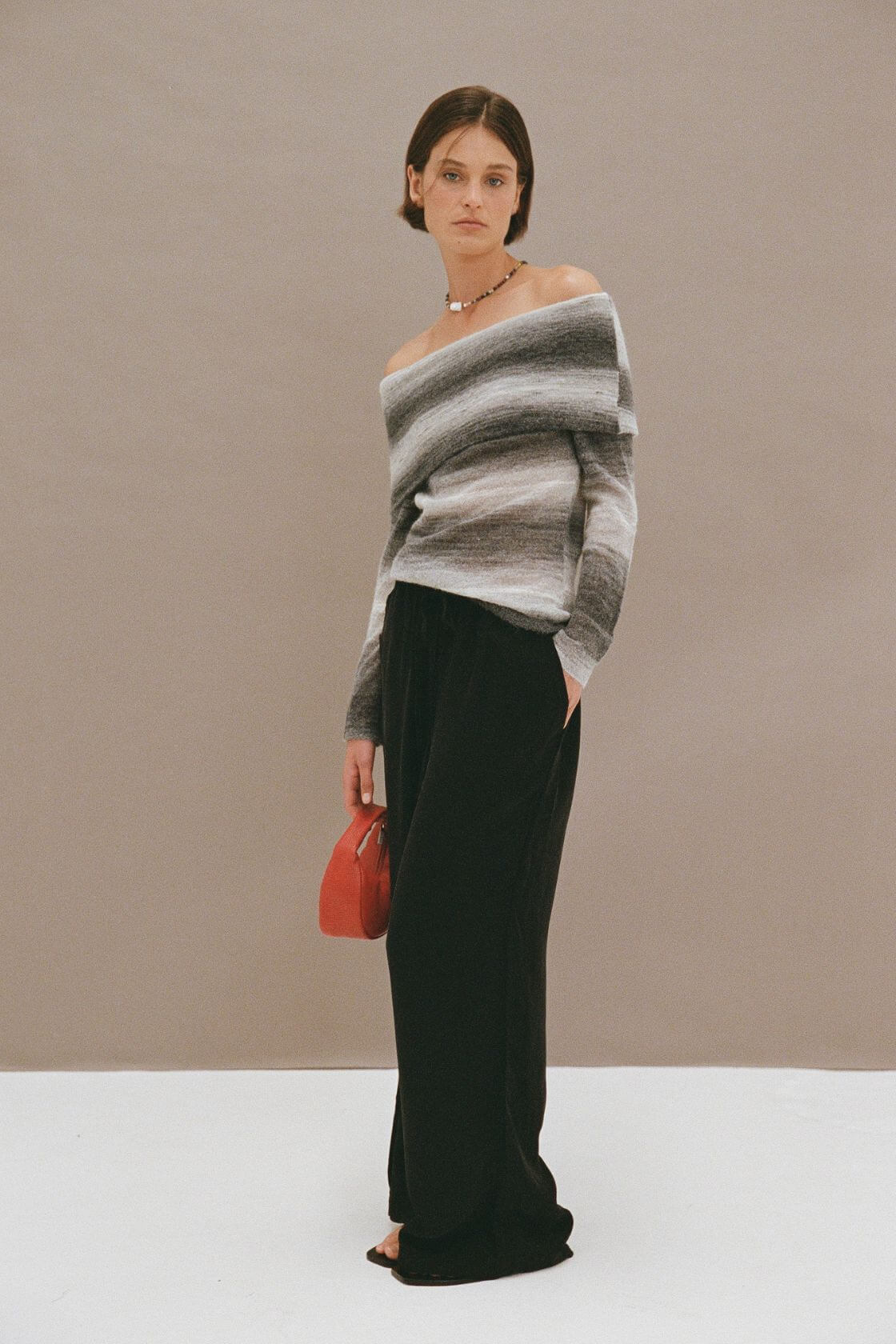 Off shoulder ombre knit top in grey tones styled with black wide leg pants and red mini bag