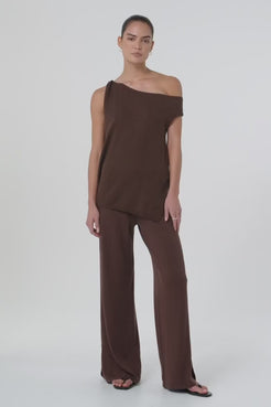 Short video showing model walking and turning in brown wide-leg cotton knit pants with elastic waistband and side splits, styled with a matching one-shoulder top. The lightweight knit fabric moves fluidly, highlighting the breathable, relaxed fit designed for warm-weather dressing and sustainable co-ord styling