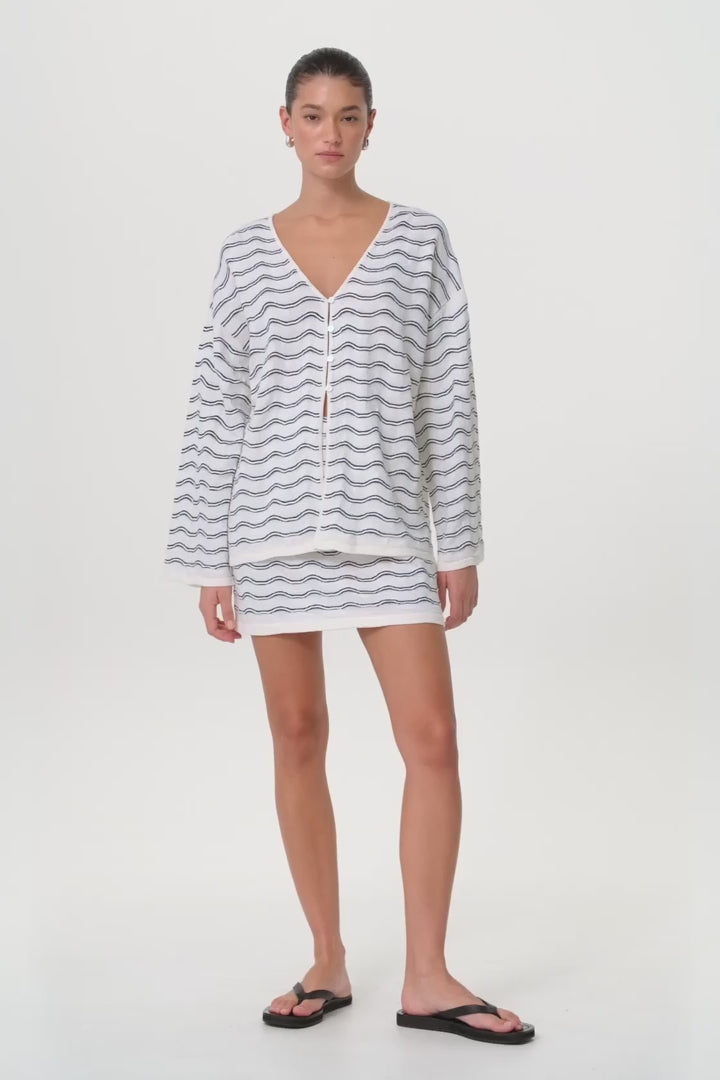 Model moves in matching wave knit mini skirt and sweater, showing texture, drape, and elastic waistband in motion.