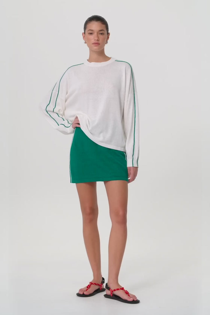 Model moves in green knit mini skirt with drawcord waist and stripe detail, styled with relaxed white knit top.
