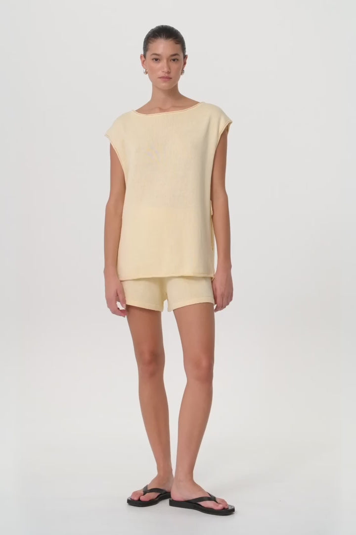 Model moves in relaxed linen shorts and matching top in butter tone, showing soft drape, side pleats, and breathable summer texture.