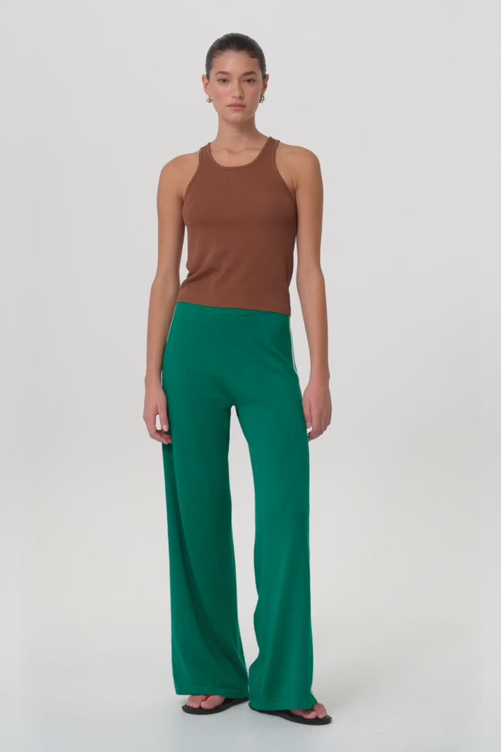 Model moves in fitted clay ribbed tank and green pants, showing sculpted shape, racer cut, and breathable stretch in motion.