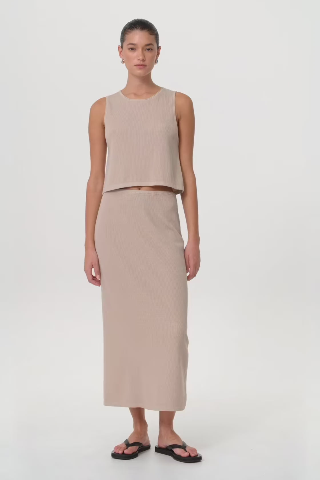 Model in motion wearing taupe knit tank and matching skirt set, highlighting flared hem, rolled edges and breathable movement through seasonal transitions.