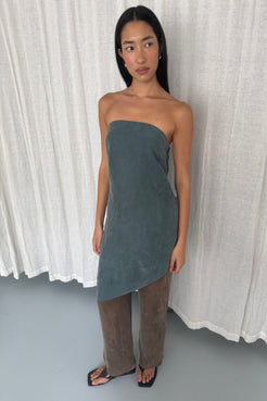 model wears the rhea dress in teal with the maisie pants in espresso against a white curtain background